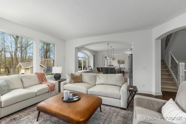 living room featuring arched walkways, baseboards, stairs, and wood finished floors