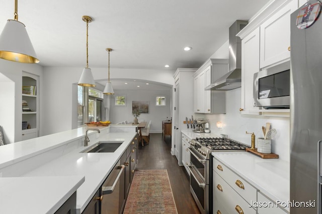 kitchen featuring dark wood finished floors, a sink, light countertops, stainless steel appliances, and wall chimney exhaust hood