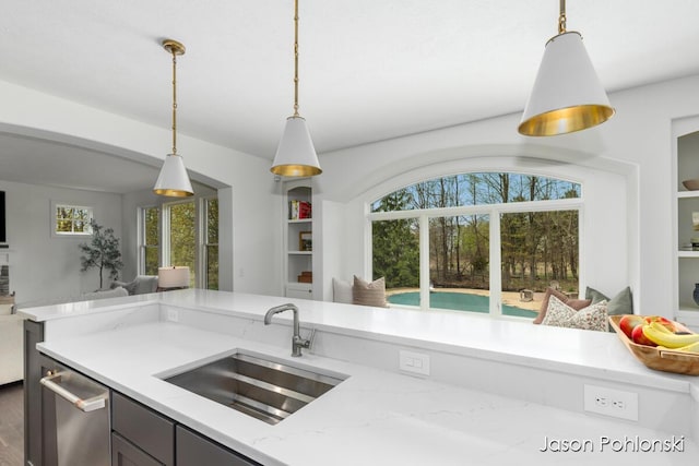 kitchen featuring decorative light fixtures, stainless steel dishwasher, a sink, light stone counters, and open floor plan