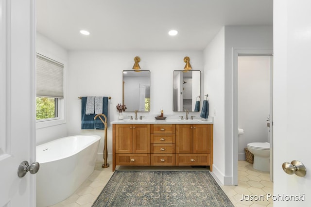bathroom with double vanity, a sink, a freestanding bath, and toilet