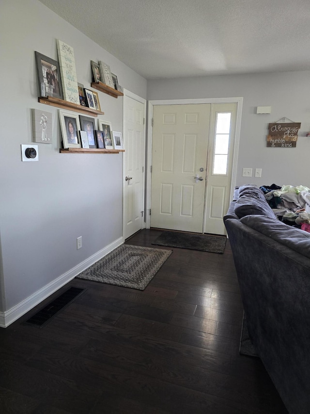 foyer featuring baseboards, dark wood-type flooring, a textured ceiling, and visible vents