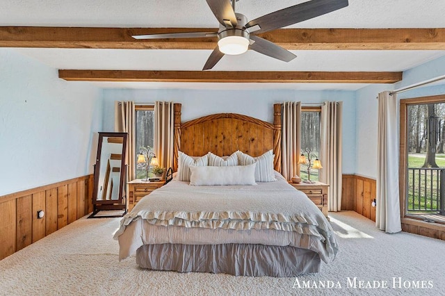 carpeted bedroom featuring beamed ceiling, wood walls, wainscoting, and multiple windows