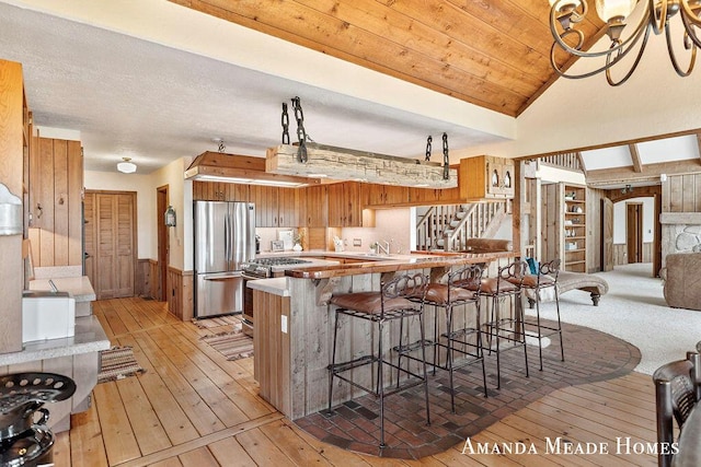 kitchen with brown cabinets, wood walls, a peninsula, stainless steel appliances, and light wood-style flooring