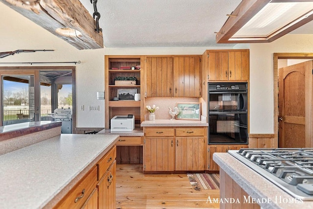 kitchen with light wood-style floors, dobule oven black, a textured ceiling, light countertops, and stainless steel gas stovetop