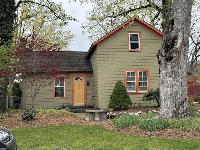traditional-style house featuring a shingled roof, a front lawn, and fence