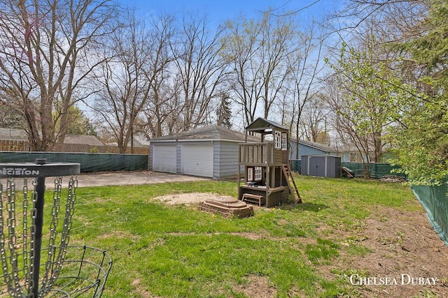 view of yard featuring an outdoor structure, fence, a playground, a storage shed, and a detached garage