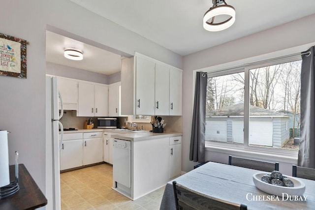 kitchen with light countertops, a sink, white cabinets, a peninsula, and white appliances