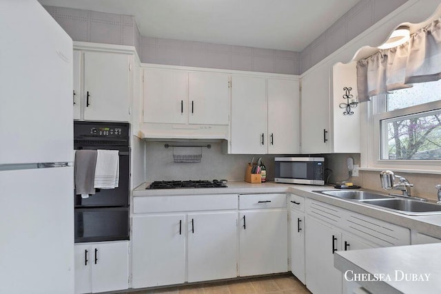 kitchen with a sink, light countertops, white cabinets, black appliances, and a warming drawer