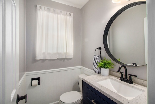 half bathroom with vanity, a wainscoted wall, a wealth of natural light, and toilet