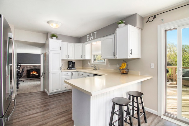 kitchen featuring a peninsula, a breakfast bar area, stainless steel refrigerator with ice dispenser, dark wood-type flooring, and a sink