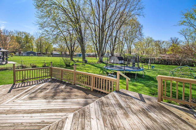 deck with a lawn, a trampoline, and fence