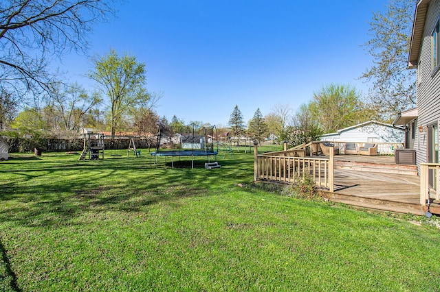 view of yard with a trampoline, a playground, a wooden deck, and fence