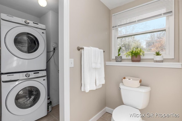 bathroom featuring toilet, stacked washer and dryer, tile patterned floors, and baseboards