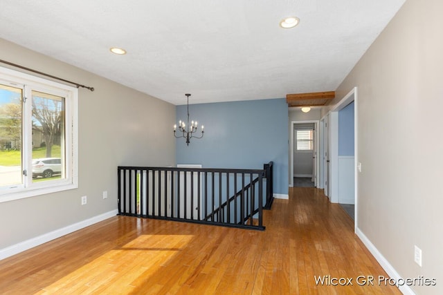 empty room featuring recessed lighting, baseboards, an inviting chandelier, and wood finished floors