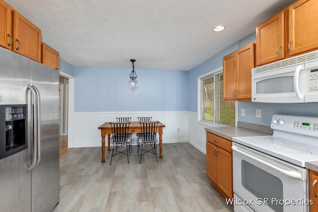 kitchen featuring a wainscoted wall, light wood finished floors, white appliances, and brown cabinetry