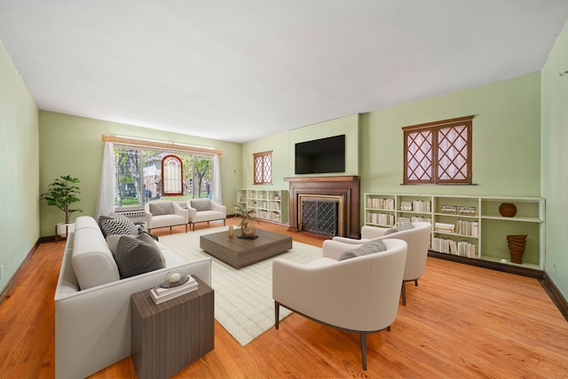 living room featuring baseboards, a fireplace with flush hearth, and wood finished floors