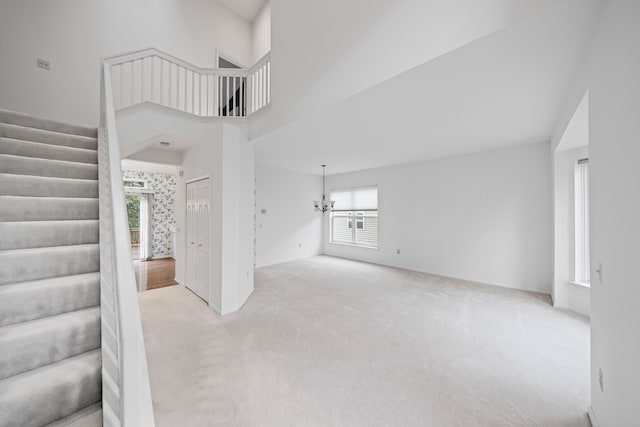 unfurnished living room featuring stairs, carpet, a notable chandelier, a high ceiling, and baseboards