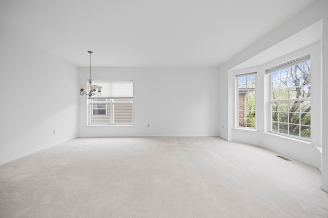carpeted empty room with baseboards, an inviting chandelier, and visible vents