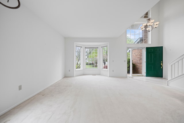 unfurnished living room with a chandelier, a high ceiling, carpet floors, and baseboards