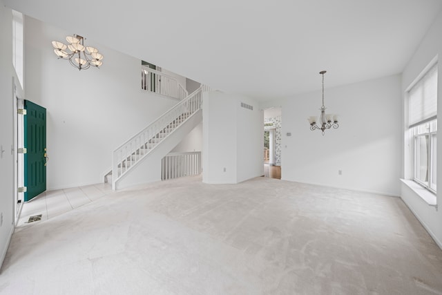 unfurnished living room with carpet flooring, a chandelier, visible vents, and stairs