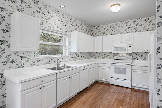 kitchen with a sink, white appliances, hardwood / wood-style floors, white cabinetry, and wallpapered walls