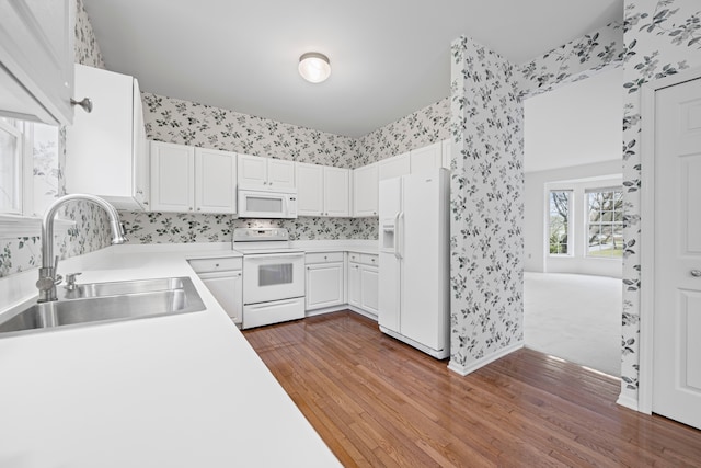 kitchen with a sink, white appliances, dark wood-style flooring, light countertops, and wallpapered walls