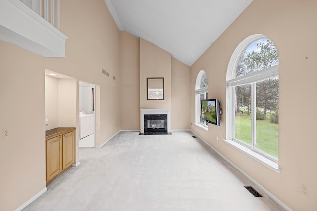 unfurnished living room with a healthy amount of sunlight, visible vents, a high end fireplace, and high vaulted ceiling