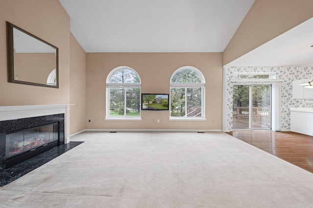 unfurnished living room featuring vaulted ceiling, baseboards, carpet floors, and a high end fireplace