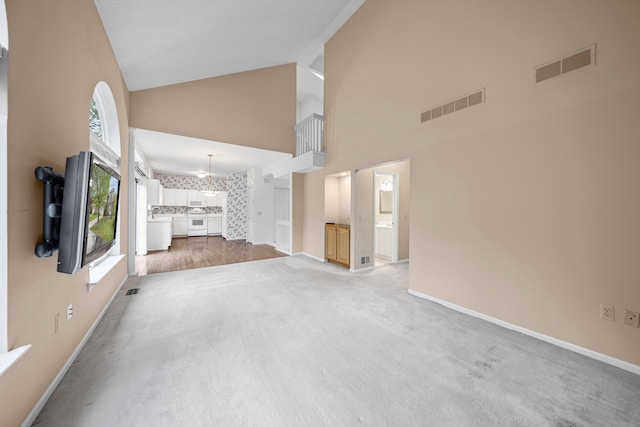 unfurnished living room with a notable chandelier, visible vents, light carpet, and high vaulted ceiling
