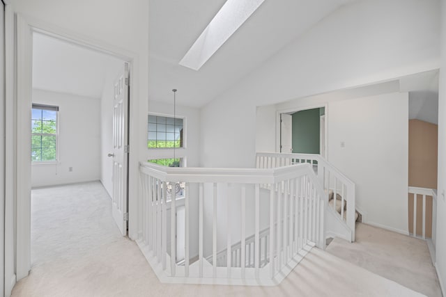 hallway featuring baseboards, lofted ceiling with skylight, carpet flooring, and an upstairs landing
