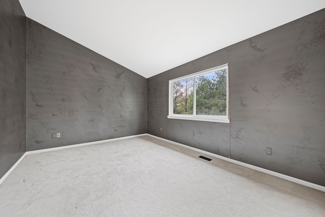 carpeted empty room featuring vaulted ceiling, baseboards, and visible vents