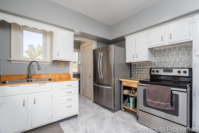 kitchen with white cabinets, appliances with stainless steel finishes, a sink, butcher block countertops, and backsplash