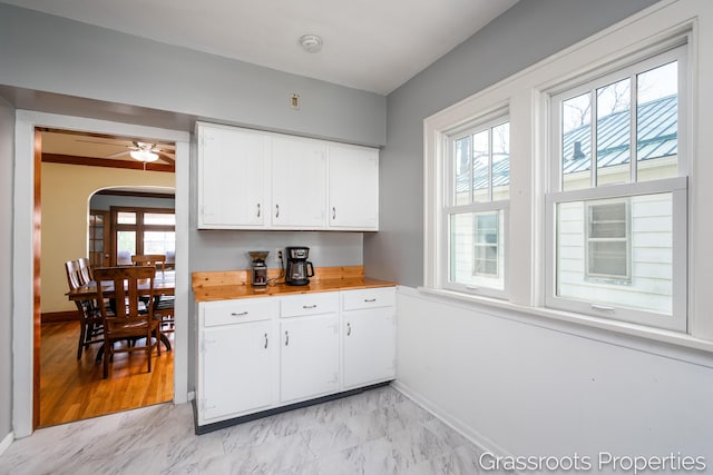 kitchen featuring light countertops, baseboards, white cabinets, and arched walkways