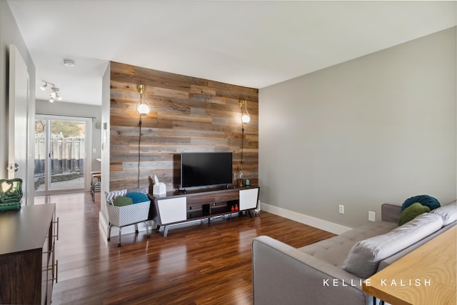 living room featuring baseboards, wood walls, an accent wall, and wood finished floors