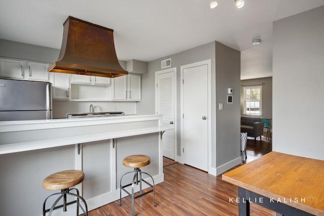 kitchen with dark wood-style flooring, light countertops, a kitchen breakfast bar, freestanding refrigerator, and island exhaust hood