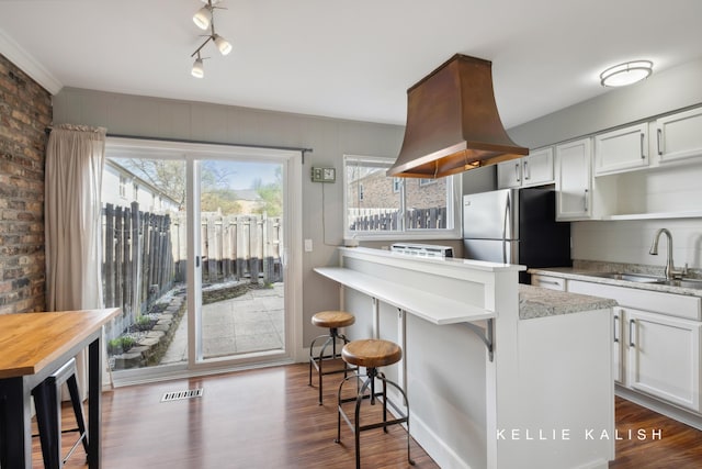 kitchen with a sink, a kitchen breakfast bar, dark wood-style floors, and freestanding refrigerator