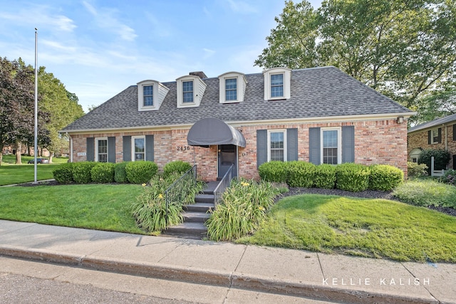 view of front of house featuring brick siding, a shingled roof, and a front yard