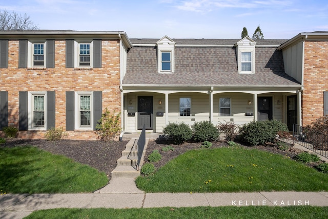 view of front of property with a porch, brick siding, roof with shingles, and a front lawn