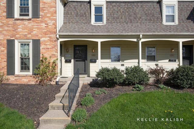 entrance to property with a porch, roof with shingles, and brick siding