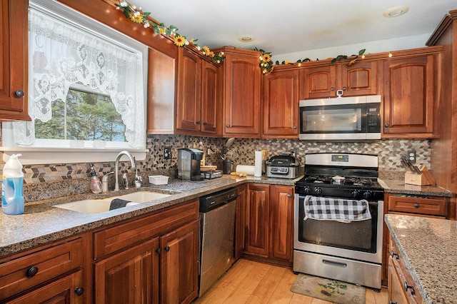 kitchen with light wood-type flooring, light stone counters, a sink, backsplash, and stainless steel appliances