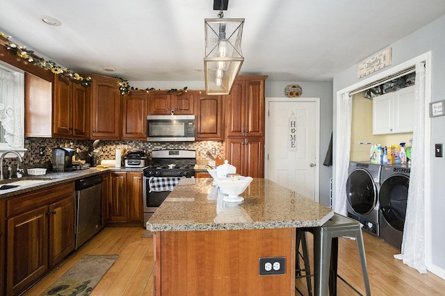 kitchen featuring a kitchen island, light wood-type flooring, washer and clothes dryer, a sink, and appliances with stainless steel finishes