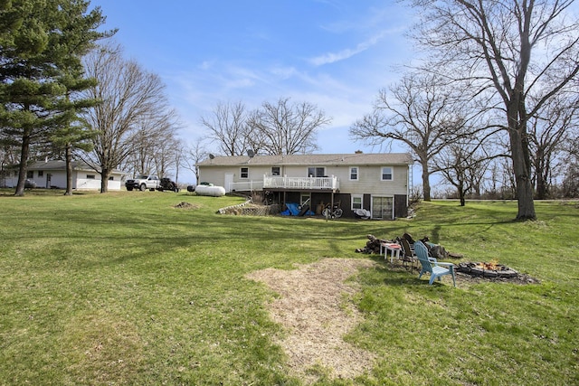 back of property featuring a yard, a wooden deck, and an outdoor fire pit