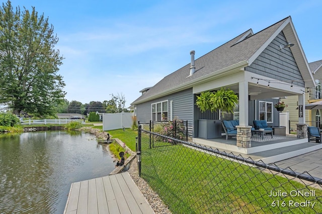 rear view of property with fence, roof with shingles, a water view, a patio area, and a yard