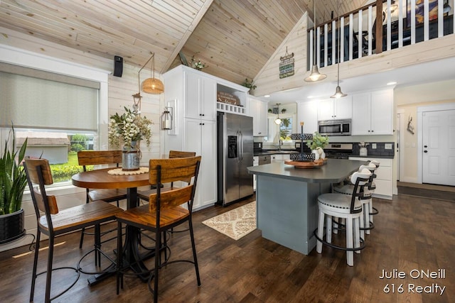 kitchen with dark countertops, appliances with stainless steel finishes, a sink, a center island, and white cabinetry