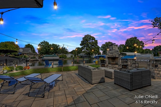 patio terrace at dusk with fence, an outdoor living space with a fireplace, an outdoor kitchen, area for grilling, and a water view