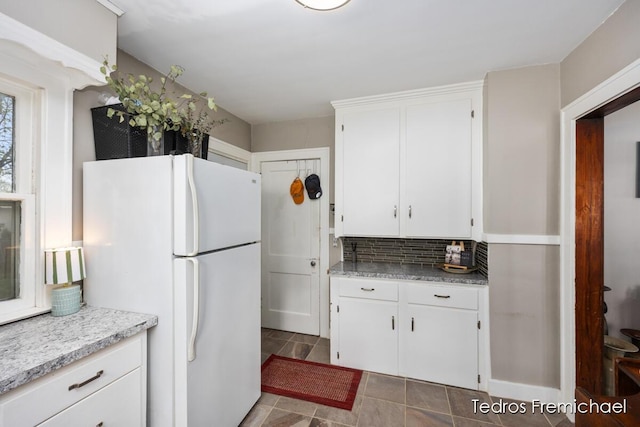 kitchen with freestanding refrigerator, white cabinetry, and decorative backsplash