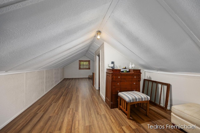 additional living space with a textured ceiling, vaulted ceiling, and wood finished floors