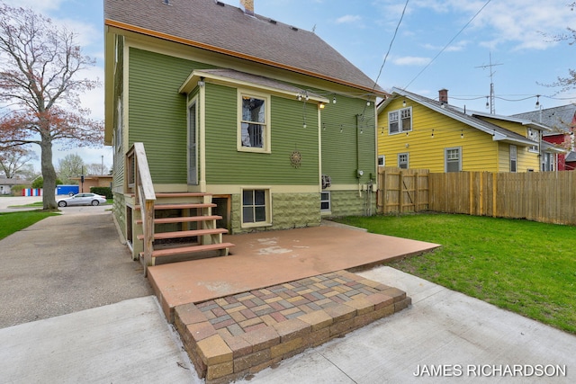 rear view of property featuring fence, a patio, a shingled roof, and a lawn