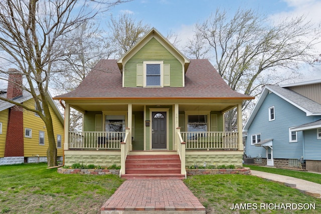 bungalow with a shingled roof, covered porch, and a front yard