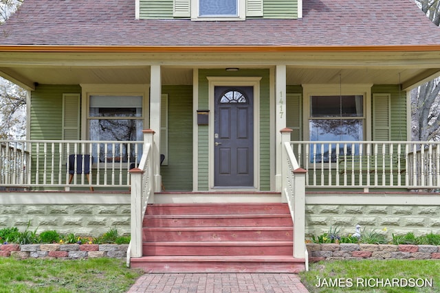 view of exterior entry with covered porch and a shingled roof
